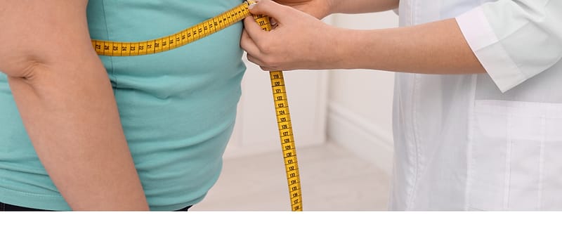 A clinician measuring a patient’s waist with a tape measure.