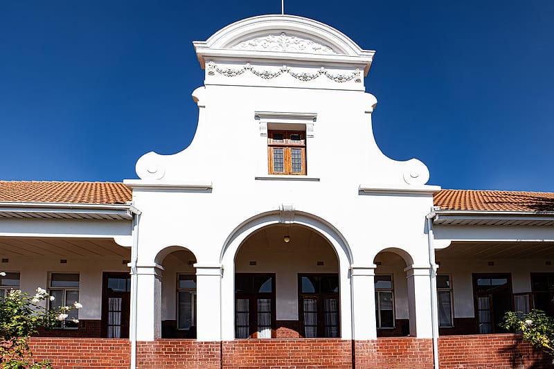 The white Cape Dutch gable of the original Zuid-Afrikaans Hospital building against a clear sky.