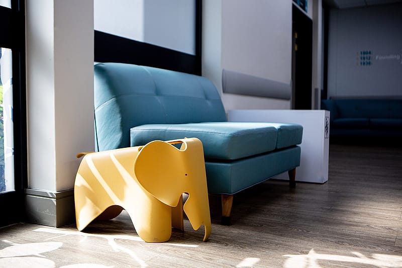 A quiet visitors’ lounge with a teal sofa beside a sunlit window.