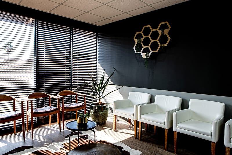 The waiting room with brass honeycomb shelving above a row of white armchairs.